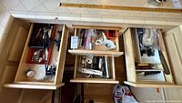 Overhead view of three drawers with assorted utensils, tools, and knives