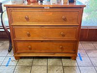 Front view showing three drawers, knob pulls, bun feet