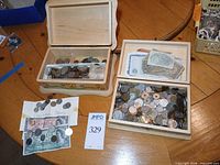 Overview of two open wooden boxes filled with assorted coins and topped with banknotes