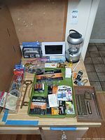 Overall lot layout on countertop showing batteries, lantern, sink strainers, luggage scale, keys, hooks and fasteners