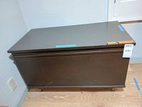 Closed view of dark brown engineered wood trunk on casters