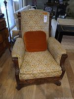 Front view of carved wood armchair with floral upholstery and orange cushion