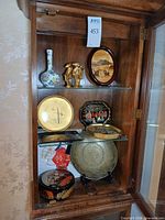 Cabinet shelves showing porcelain vase, brass elephant, brass plates, lacquer pieces