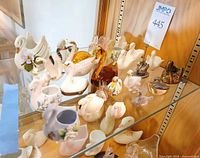 Group of porcelain, glass and metal swan figurines on glass shelf