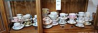 Cabinet shelf with two rows of assorted floral teacups and saucers