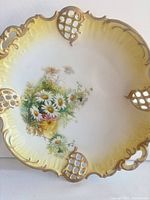 Front view of porcelain plate showing floral painting, pierced gilded rim and yellow gradient border