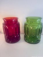 Front view of both red and green pressed glass vases