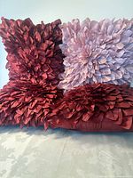 Four satin throw pillows, two burgundy two blush, showing overall 3D flower design