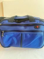 Front view showing blue nylon duffel, twin exterior zip pockets, brand badge and top handles