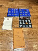 All components laid out: blue album open showing coins, black display board, tan booklet, white pamphlet