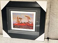 Framed lithograph with protective corner guards resting on sofa