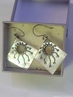 Front view of earrings showing mother of pearl squares and sterling sunburst design