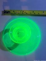 Candle holder glowing bright green under UV light with measuring tape showing scale