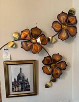 Front view of metal flower wall art mounted above framed print