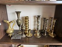 Shelf view showing all brass candlesticks, pitcher, vase, incense burner, letter holder
