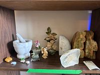 Shelf view with mortar-pestle, jade duck, bone figurine, glass bonsai, agate slice bookend, onyx bookend pair, resin flower paperweight
