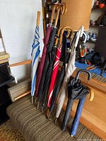 Group of eight umbrellas leaning on couch, showing colours and handle types