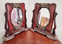 two identical ornate wood frames with oval mirrors shown front view on tabletop
