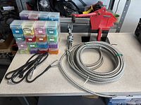All lot items on table: storage boxes, conduit coil, bungees, drill jig, red cutter