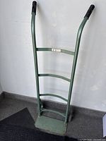Front view of green hand truck dolly showing frame, handle grips, wheels, and load plate