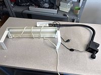 White fluorescent tube task light with brackets alongside black gooseneck clamp lamp on tabletop
