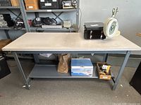 Front view showing full length of table, laminate top, metal legs, lower shelf