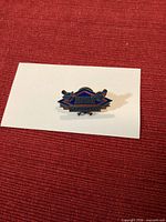 Front view of enamel pin placed on white card against red background