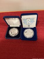 Both medallions in open blue velvet cases showing obverse designs and certificate card