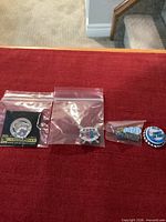 Front view of three pins in bags and one bottle cap