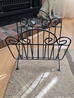 Front view of black wrought iron scrollwork magazine rack standing on carpet