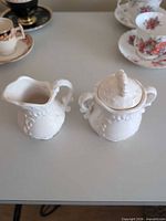 Creamer and covered sugar bowl side by side showing relief pattern and overall condition