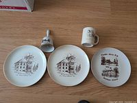 Group shot of two plates, bell, mug showing front graphics and gold trim
