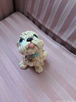 Front view of seated cream puppy figurine with blue eyes and collar