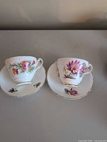 Front view of both teacup and saucer sets displaying floral patterns and gold trim