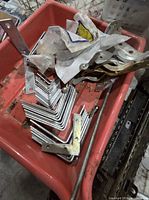 Close-up of red bin showing stack of metal L-brackets, steel braces and threaded rod