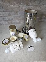 Group shot of all items: mirrored electric wax warmer lamp, two ceramic plug-in night lights, jar candle and tin candles