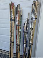 Full view of three strapped bundles of right-handed hockey sticks leaning against garage door