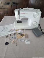 Singer Prelude machine with foot pedal, power cord, accessory kit and manual displayed on table