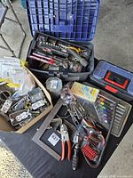 overview of totes, toolboxes, hand tools and box of electrical supplies on table
