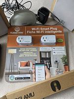 Close-up of sealed Wi-Fi smart plug two-pack with Sylvania receiver and part of speaker visible