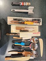 Full lot overview showing meat mallet, knives in trays, utensils, measuring spoons, knife guard, spatula