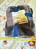Folded brown plush blanket with label and blue strap on floral rug