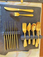 Gold-tone skewers, dinner knife, one dinner fork, cluster of gold-tone forks and spoons in foam holder