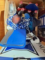 Top view of lot inside box showing wine glass, Coca-Cola bottles, basketball ornament, plush mascot, pom-poms, pouch and signage