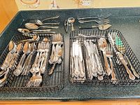 Overall view of two baskets filled with assorted ornate flatware and separate serving pieces on countertop