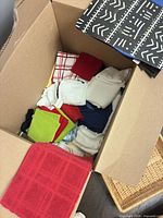 Open box showing assorted cotton towels in various colors and a black patterned mat
