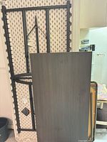 Three folded tables leaning: white plastic, dark laminate, beige card