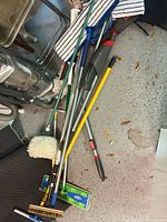 Pile of vacuum, brooms, mops, Swiffer bases and duster