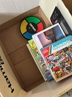 Top view of Simon game and stacked jigsaw puzzle boxes inside cardboard box