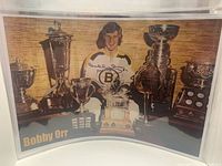 Colour poster with Orr seated among trophies, visible signature